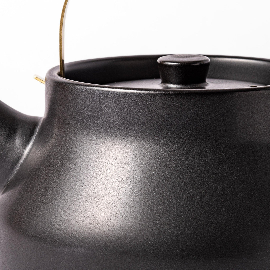 Black ceramic stovetop kettle with a curved silhouette and sleek brass handle, perfect for brewing tea with both elegance and everyday function.