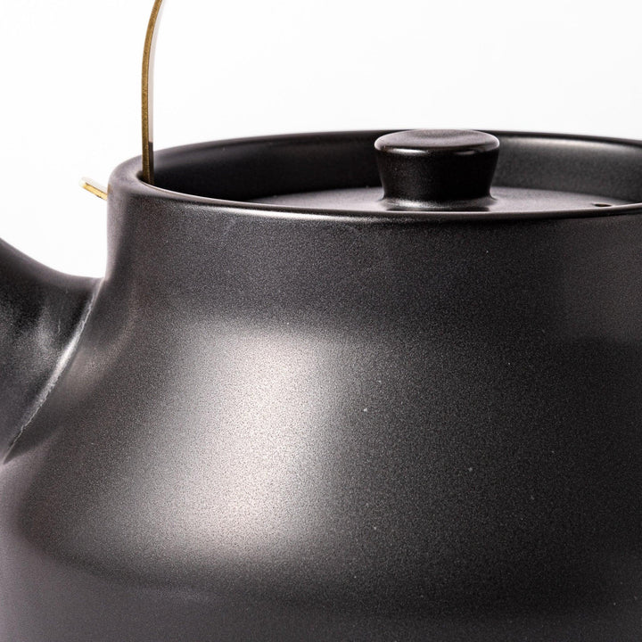 Black ceramic stovetop kettle with a curved silhouette and sleek brass handle, perfect for brewing tea with both elegance and everyday function.