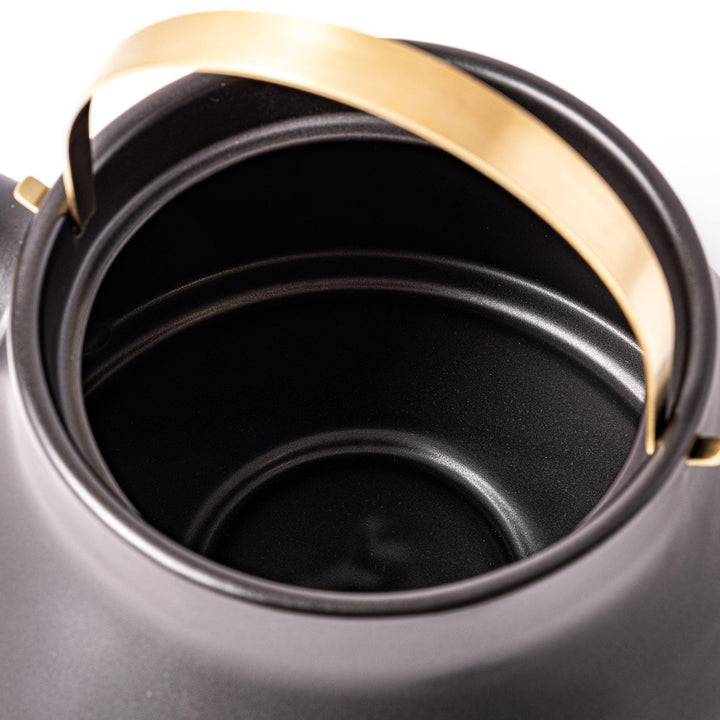 Black ceramic stovetop kettle with a curved silhouette and sleek brass handle, perfect for brewing tea with both elegance and everyday function.