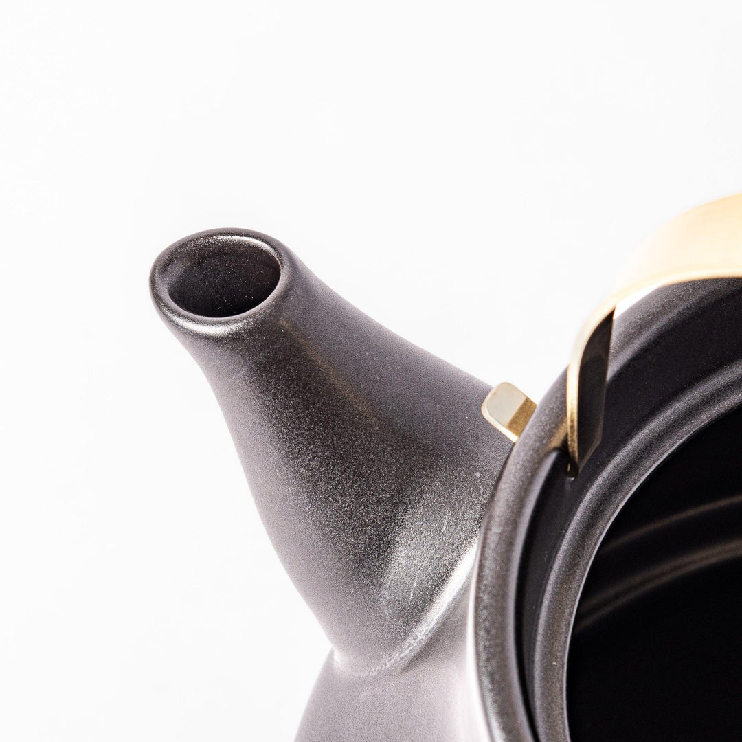 Black ceramic stovetop kettle with a curved silhouette and sleek brass handle, perfect for brewing tea with both elegance and everyday function.