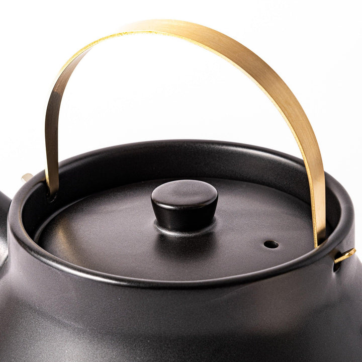 Black ceramic stovetop kettle with a curved silhouette and sleek brass handle, perfect for brewing tea with both elegance and everyday function.