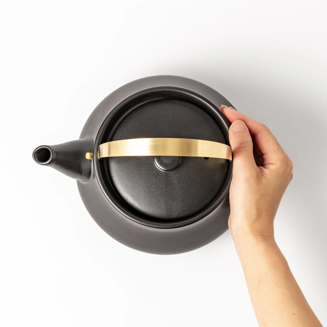 Black ceramic stovetop kettle with a curved silhouette and sleek brass handle, perfect for brewing tea with both elegance and everyday function.