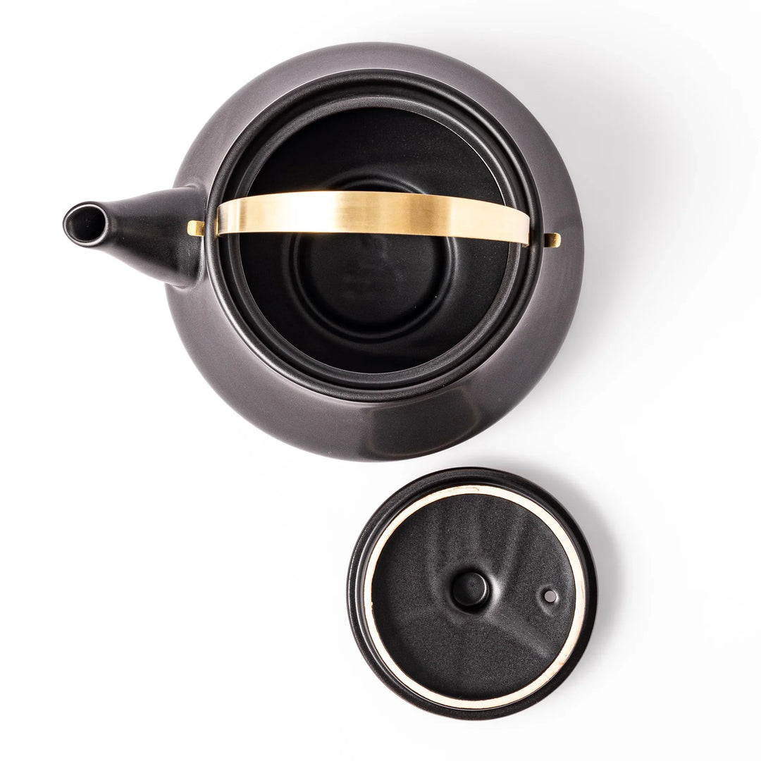 Black ceramic stovetop kettle with a curved silhouette and sleek brass handle, perfect for brewing tea with both elegance and everyday function.