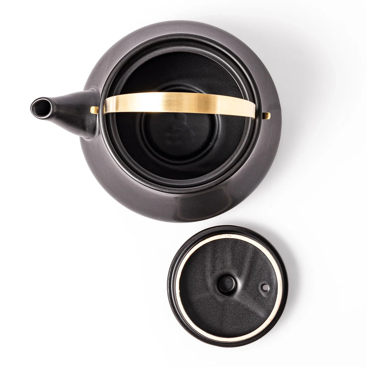 Black ceramic stovetop kettle with a curved silhouette and sleek brass handle, perfect for brewing tea with both elegance and everyday function.