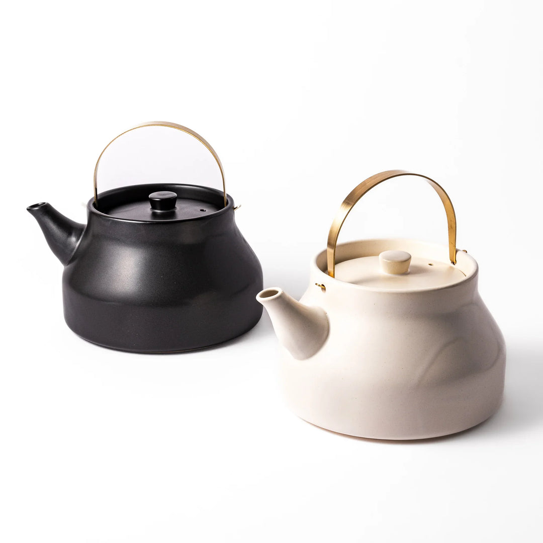 Ceramic stovetop kettles in black and white with elegant brass handles, crafted for stylish tea preparation and modern Japanese kitchens.