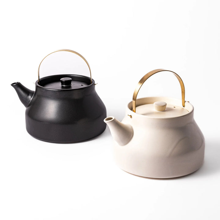 Ceramic stovetop kettles in black and white with elegant brass handles, crafted for stylish tea preparation and modern Japanese kitchens.