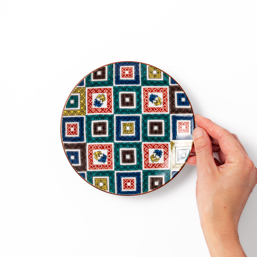 Colorful porcelain dessert plate featuring a mosaic of geometric square patterns in red, green, yellow, blue, and black with floral accents.