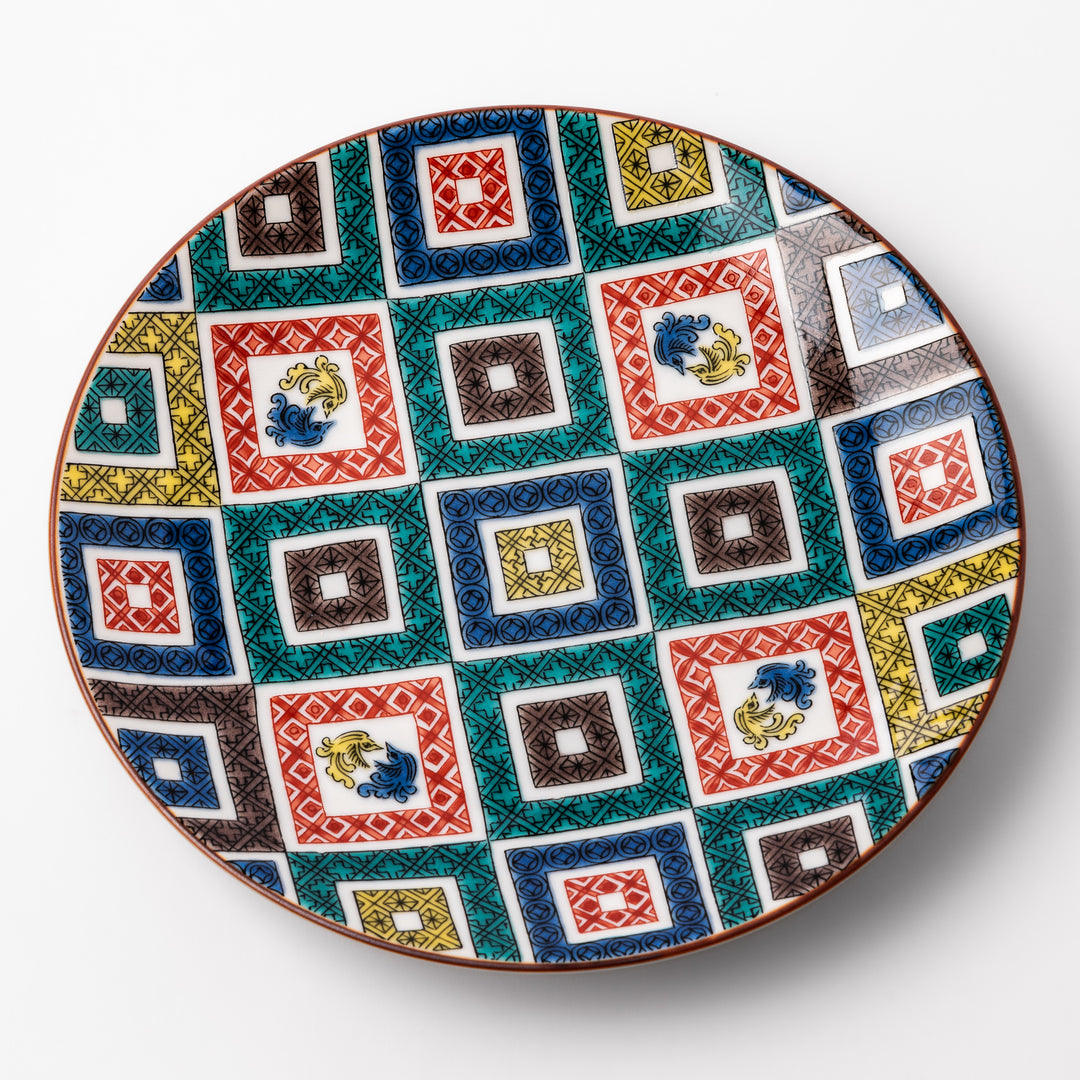 Colorful porcelain dessert plate featuring a mosaic of geometric square patterns in red, green, yellow, blue, and black with floral accents.