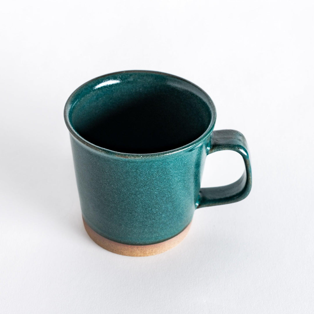 Slightly angled view of a green ceramic mug, capturing its sturdy handle and glossy green surface.