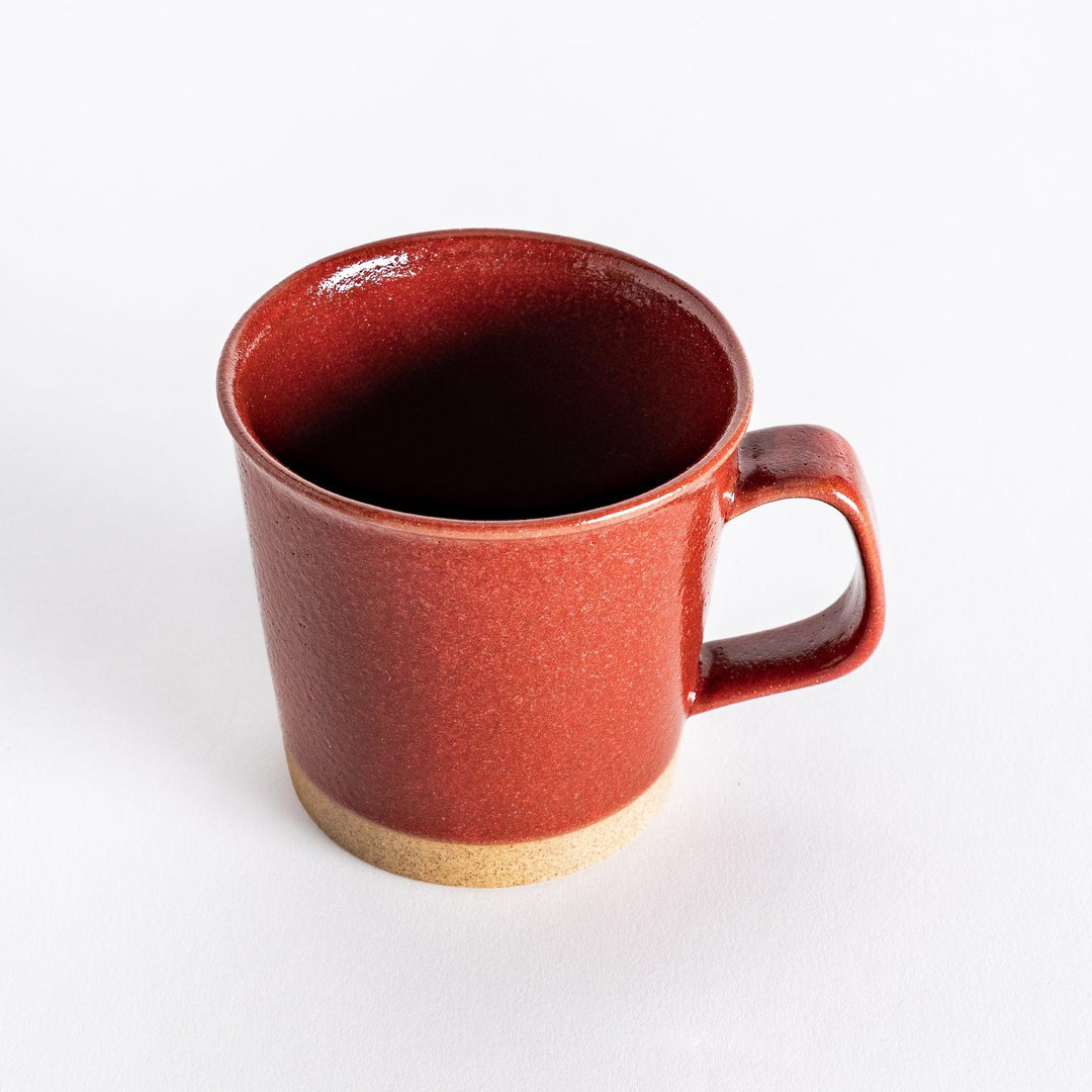 Slightly angled view of a red ceramic mug with a smooth handle and glossy red surface, emphasizing its simple and sturdy shape.