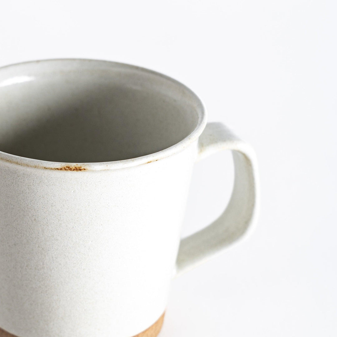 Close-up view of a white ceramic mug, showing a small worn area near the rim and a neutral-toned base, emphasizing its smooth texture and minimalist design.