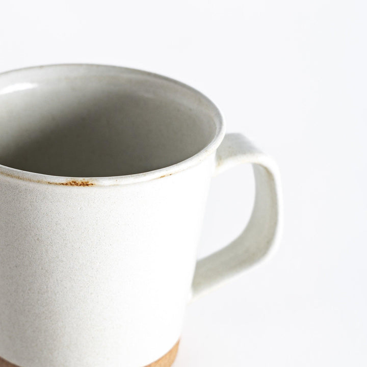 Close-up view of a white ceramic mug, showing a small worn area near the rim and a neutral-toned base, emphasizing its smooth texture and minimalist design.