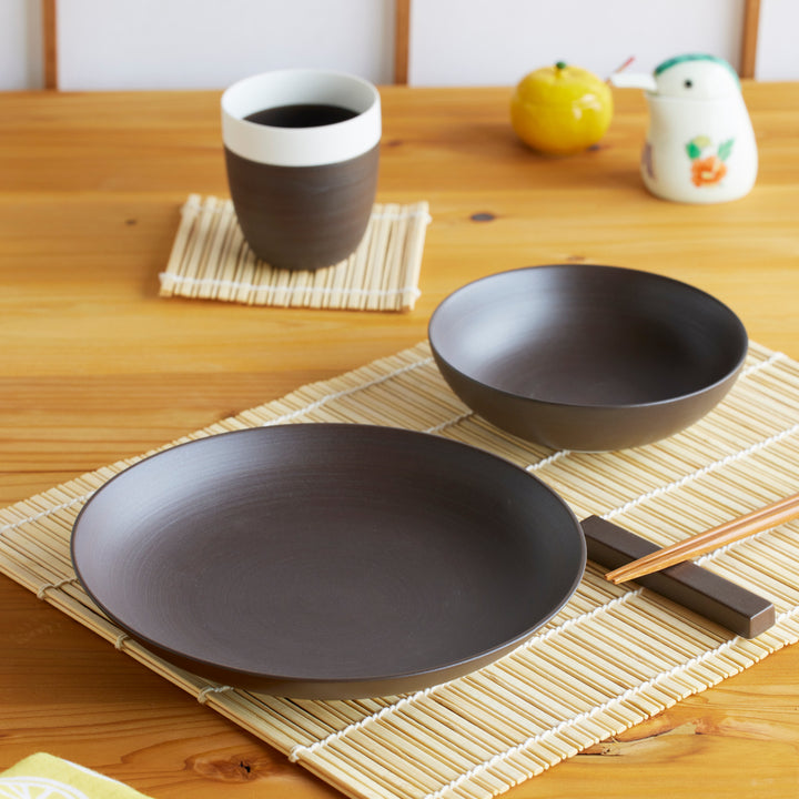 Minimalist brown dinnerware set with a plate, bowl, and cup, styled on a bamboo mat for a cozy Japandi-inspired table setting.