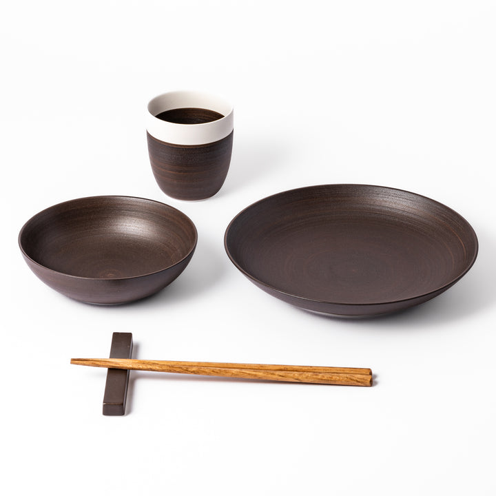 Ceramic bowl, plate, and cup set in rich brown with natural wood chopsticks and matching chopstick rest on a white background