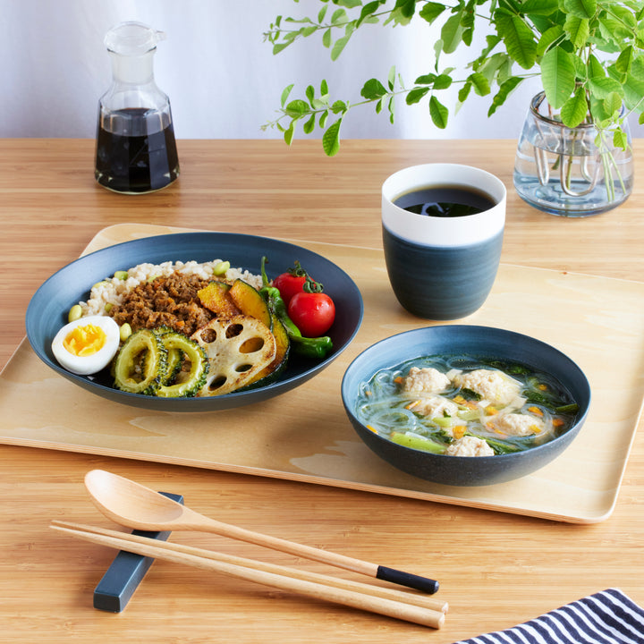 Navy blue dinnerware set with rice dish, soup bowl, and cup, paired with wooden chopsticks and spoon on a wooden tray.
