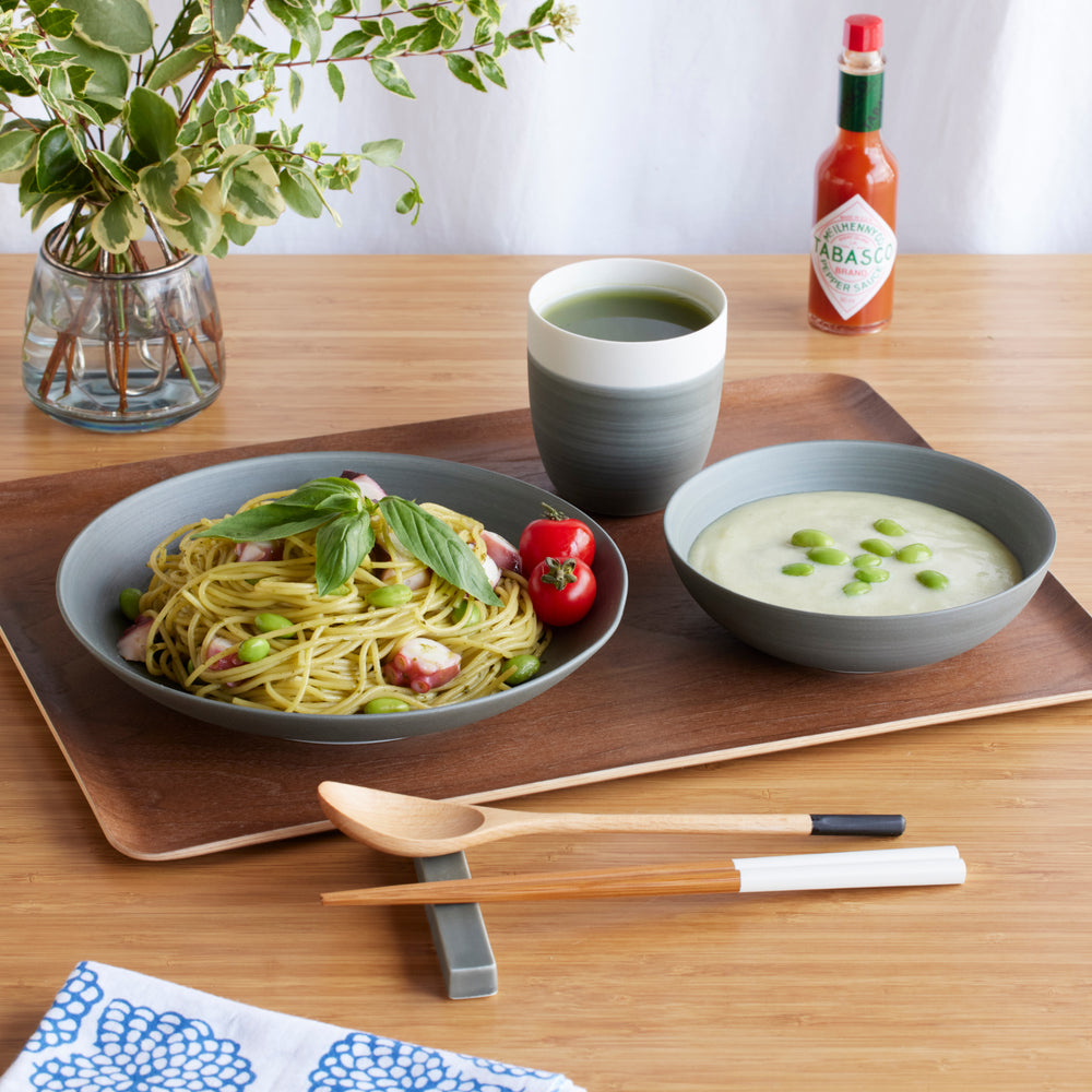 Cozy Japandi 4-Piece Dinnerware Set in gray, featuring a tea cup, pasta plate, and soup bowl, displayed on a wooden tray with a modern meal setting.