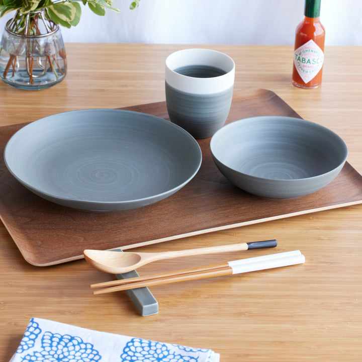 Cozy Japandi 4-Piece Dinnerware Set in gray, including a wide plate, bowl, and tea cup, arranged on a wooden tray with chopsticks and spoon.