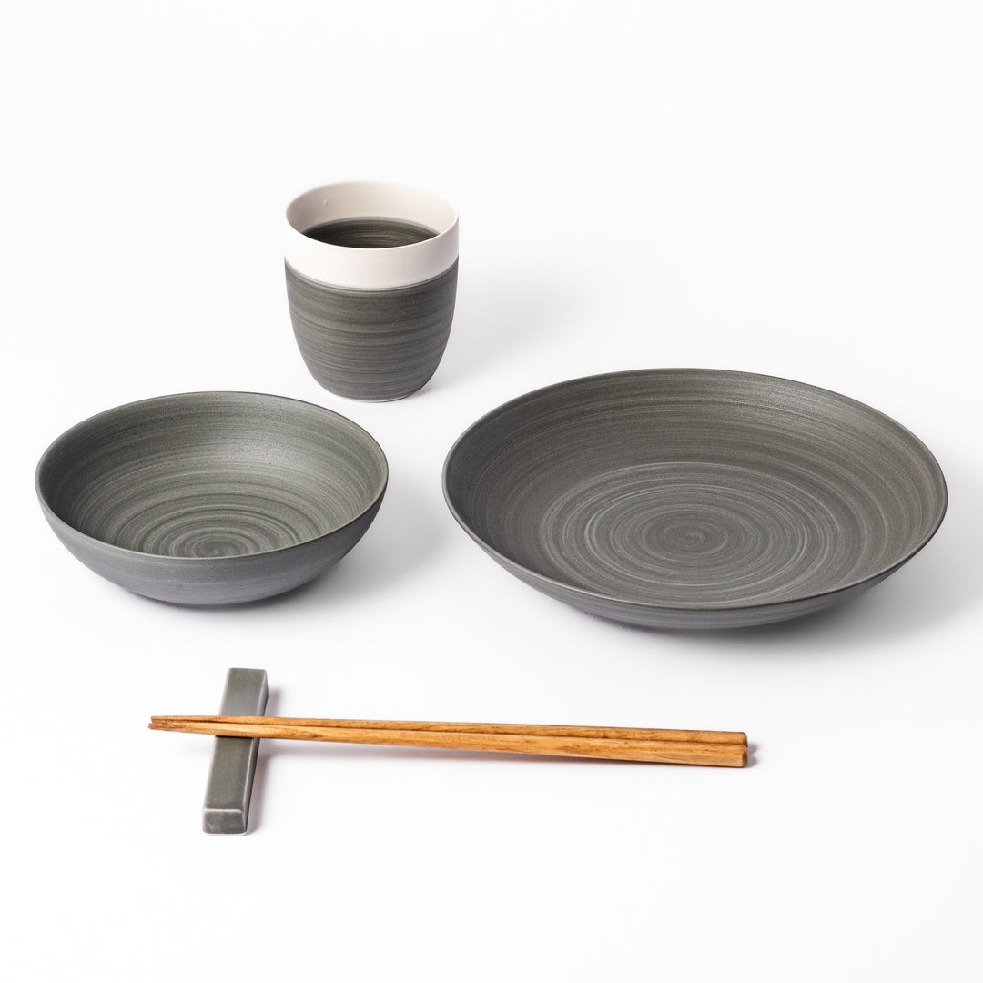 Japandi-style table setting in cool gray tones featuring a salad plate, bowl, tea cup, and chopsticks with rest.