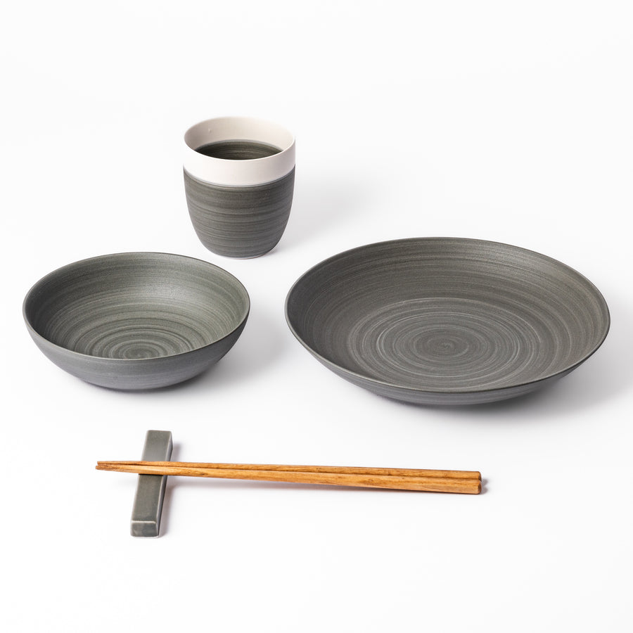 Japandi-style table setting in cool gray tones featuring a salad plate, bowl, tea cup, and chopsticks with rest.
