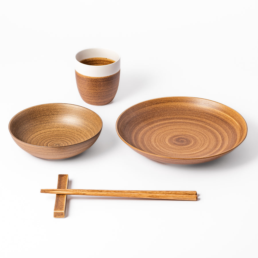 Japandi-style table setting in warm brown tones featuring a salad plate, bowl, tea cup, and chopsticks with rest.