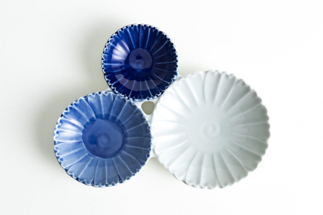 Porcelain trio dish with three connected chrysanthemum-shaped bowls in deep navy, blue, and white on a white background.