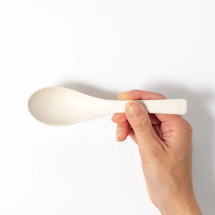 White ceramic scoop spoon with angled handle and deep, curved bowl for smooth serving of soup, stew, or curry.