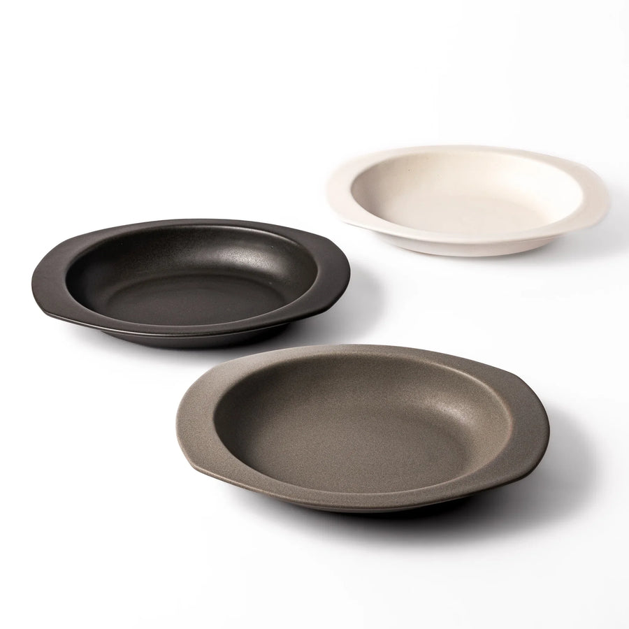 Set of three oval ceramic curry plates in black, gray, and white, featuring wide rims and deep centers for easy scooping and versatile serving.