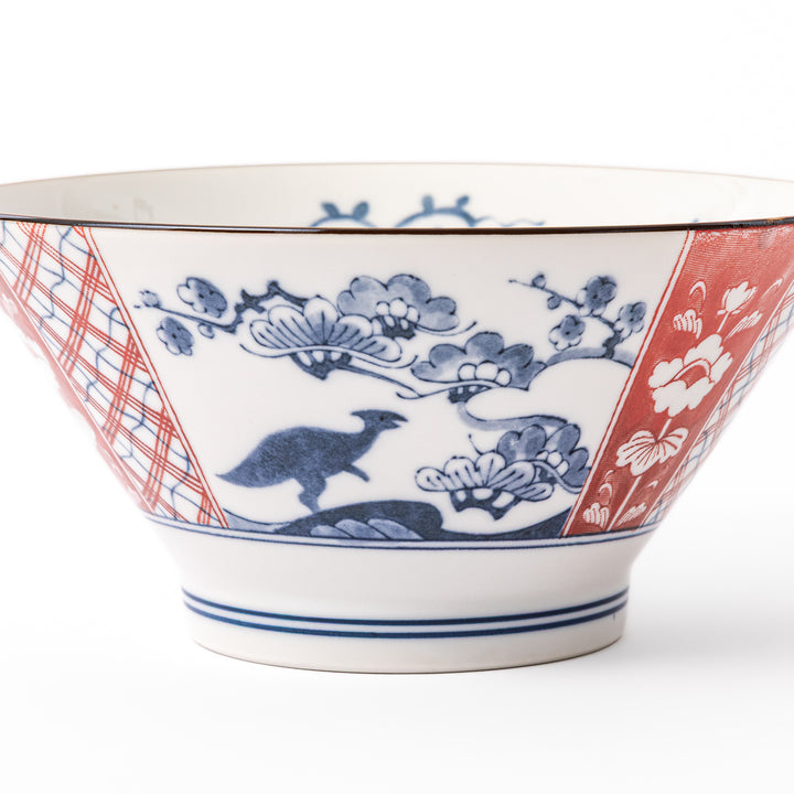 A blue red and white ceramic Japanese ramen bowl featuring a cute dinosaur silhouette amidst traditional pine and floral patterns