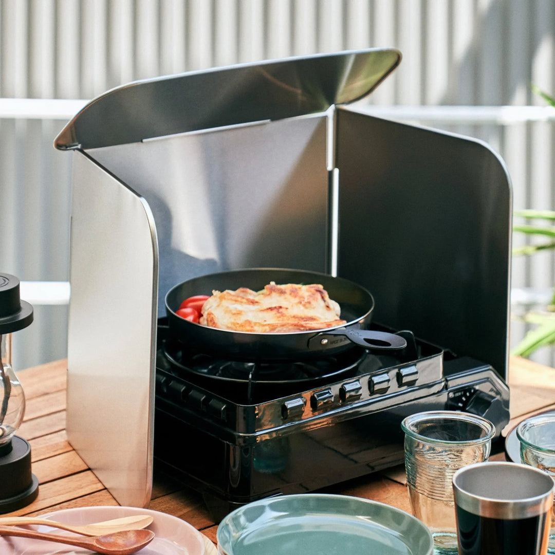 Four sided stainless steel splatter guard set up around a portable gas stove during outdoor cooking
