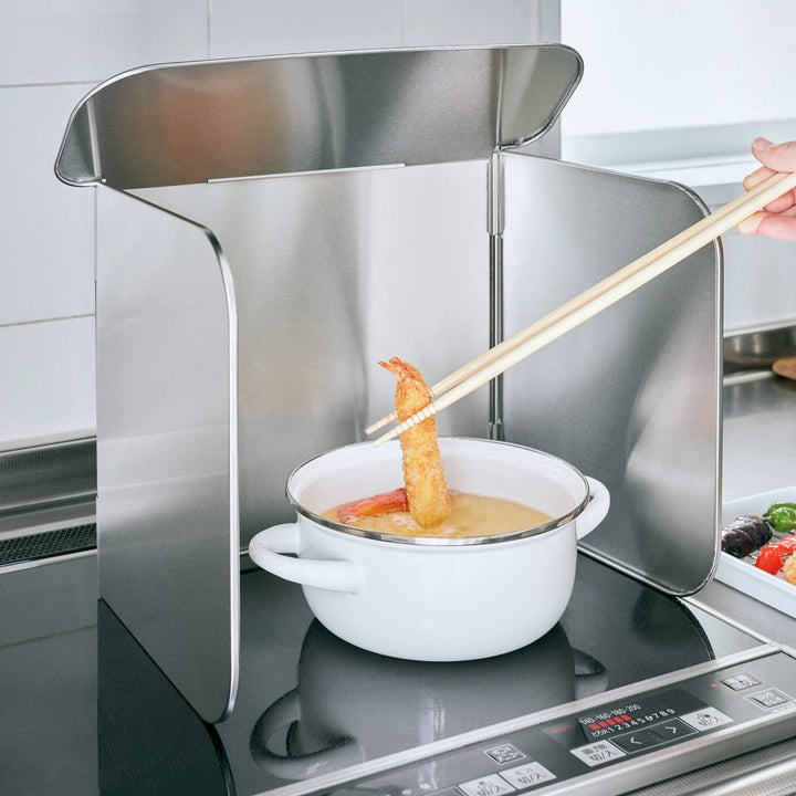 Stainless steel stove splatter guard surrounding a pot of oil while frying shrimp on an induction cooktop