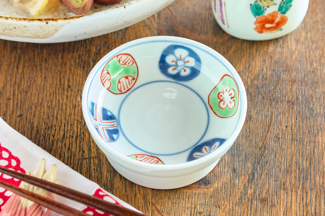 Colorful small porcelain dish with traditional Japanese patterns placed beside sashimi, chopsticks, and a bird-shaped soy sauce dispenser.