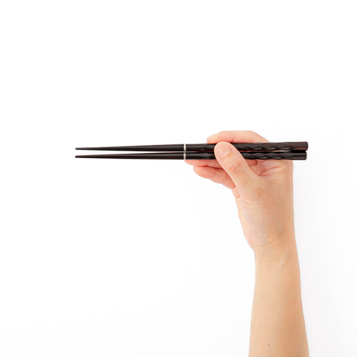 A hand holding dark wood portable Japanese travel chopsticks to showcase the comfortable nonslip textured grip