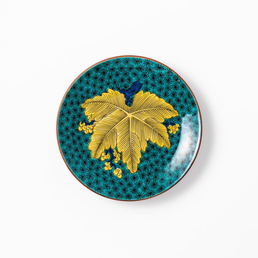 Round Kutani dessert plate with a bold golden leaf and grape motif on a turquoise background patterned with black starbursts.