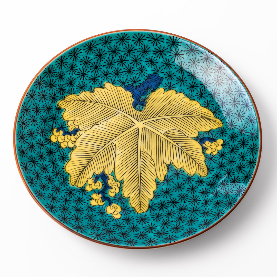 Round Kutani dessert plate with a bold golden leaf and grape motif on a turquoise background patterned with black starbursts.