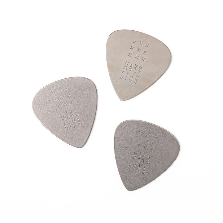 Set of three unique guitar pick shaped metal coasters in assorted finishes engraved with make line text and cross patterns