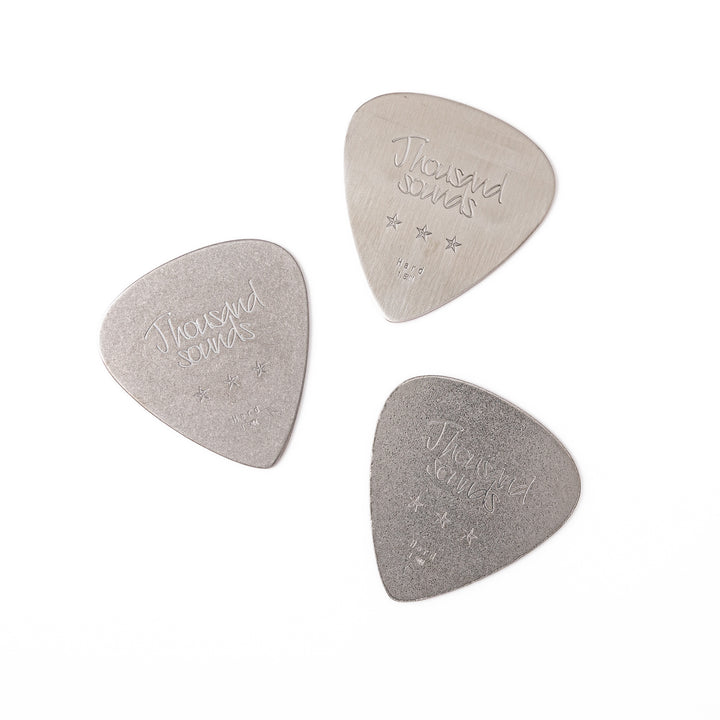 Set of three unique guitar pick shaped metal coasters in assorted finishes engraved with thousand sounds text and stars