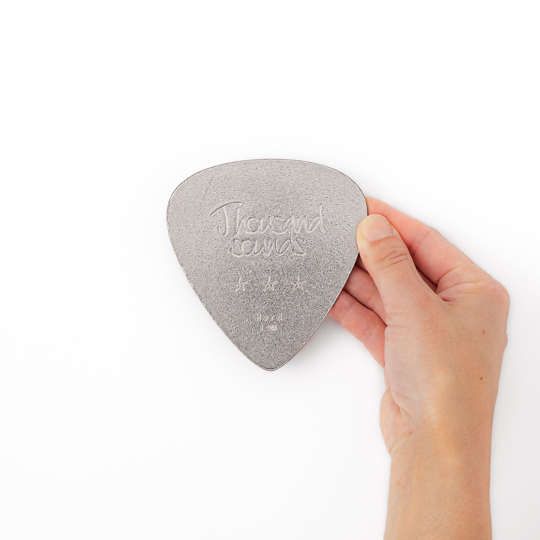 Unique guitar pick shaped metal coaster with sandblasted textured finish engraved with thousand sounds text and stars