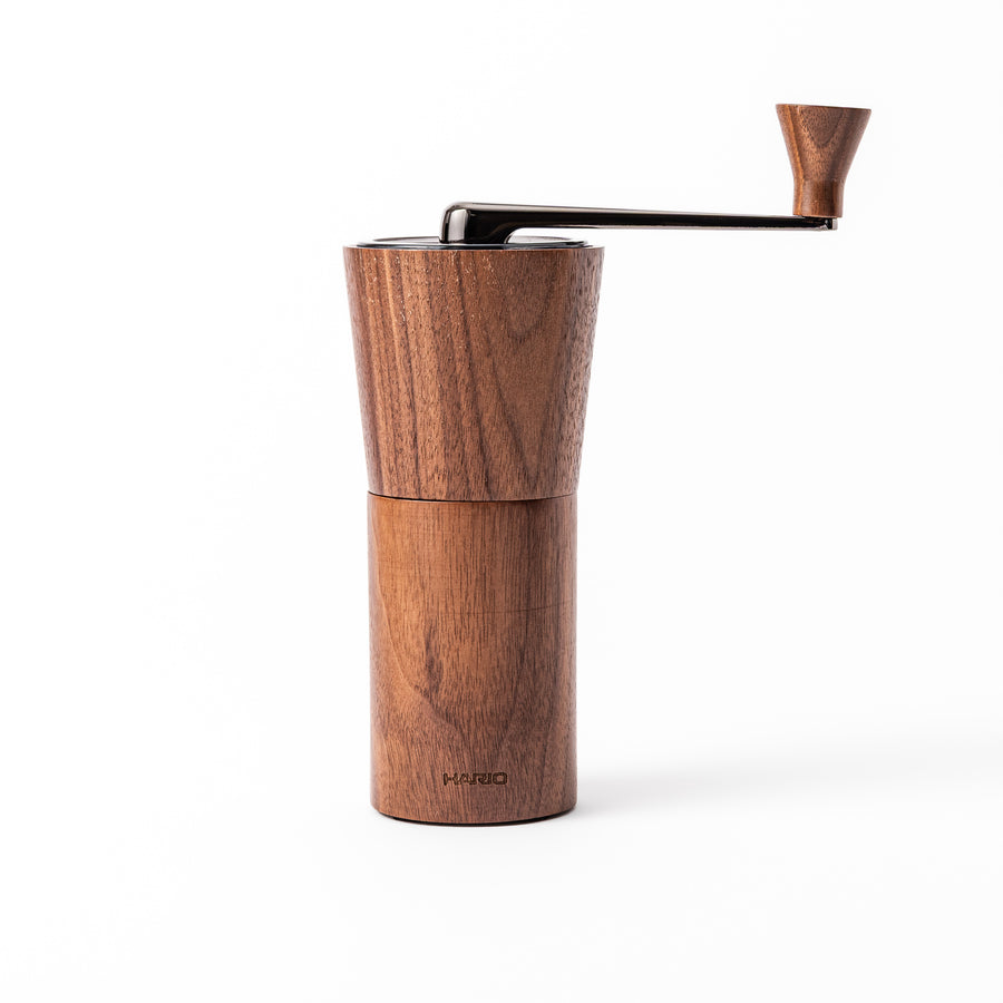 HARIO walnut wood manual coffee grinder with a hand crank, featuring a sleek natural wooden body on a white background