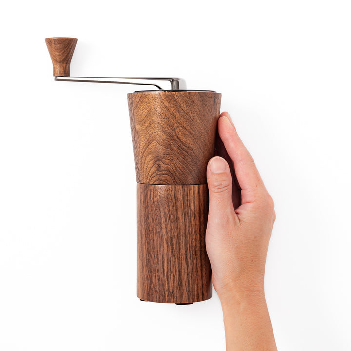 HARIO walnut wood manual coffee grinder with a hand crank, featuring a sleek natural wooden body on a white background