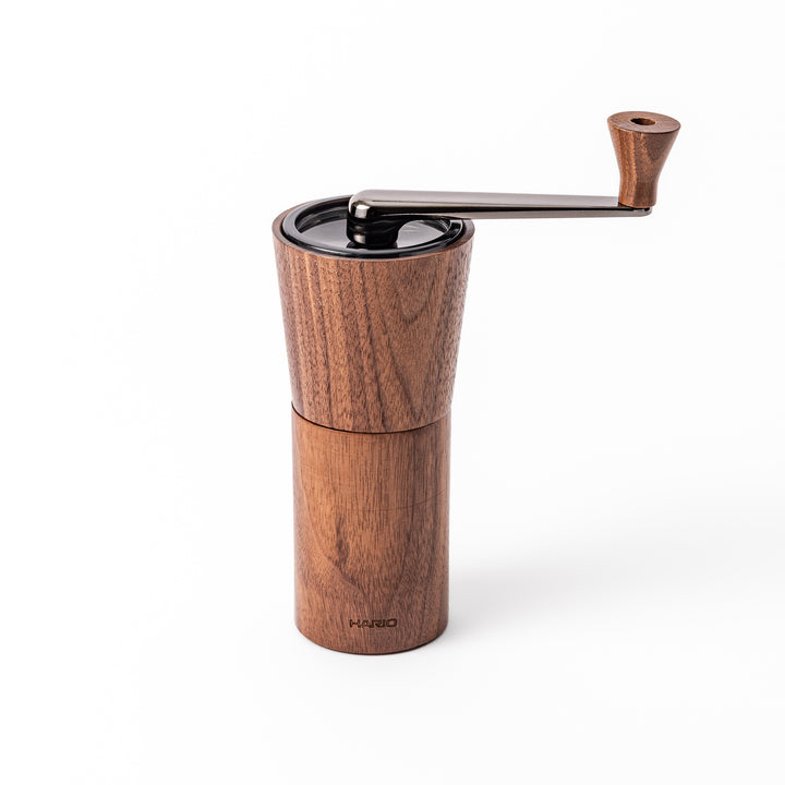 HARIO walnut wood manual coffee grinder with a hand crank, featuring a sleek natural wooden body on a white background