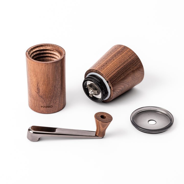 HARIO walnut wood manual coffee grinder with a hand crank, featuring a sleek natural wooden body on a white background