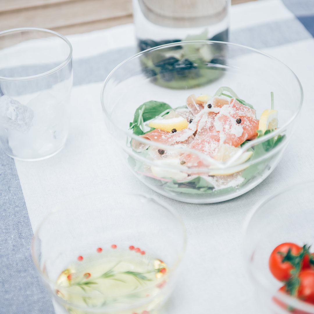 Fresh salad inside hario heatproof glass bowl near salad dressing and fruit infused water pitcher on dining table