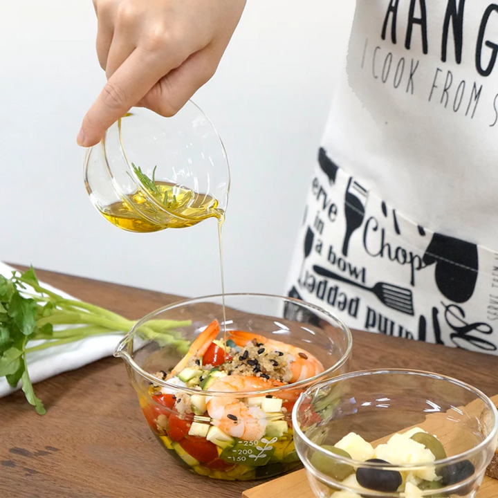 Pouring olive oil from a small hario glass lip bowl into a large mixing bowl with shrimp salad cooking preparation
