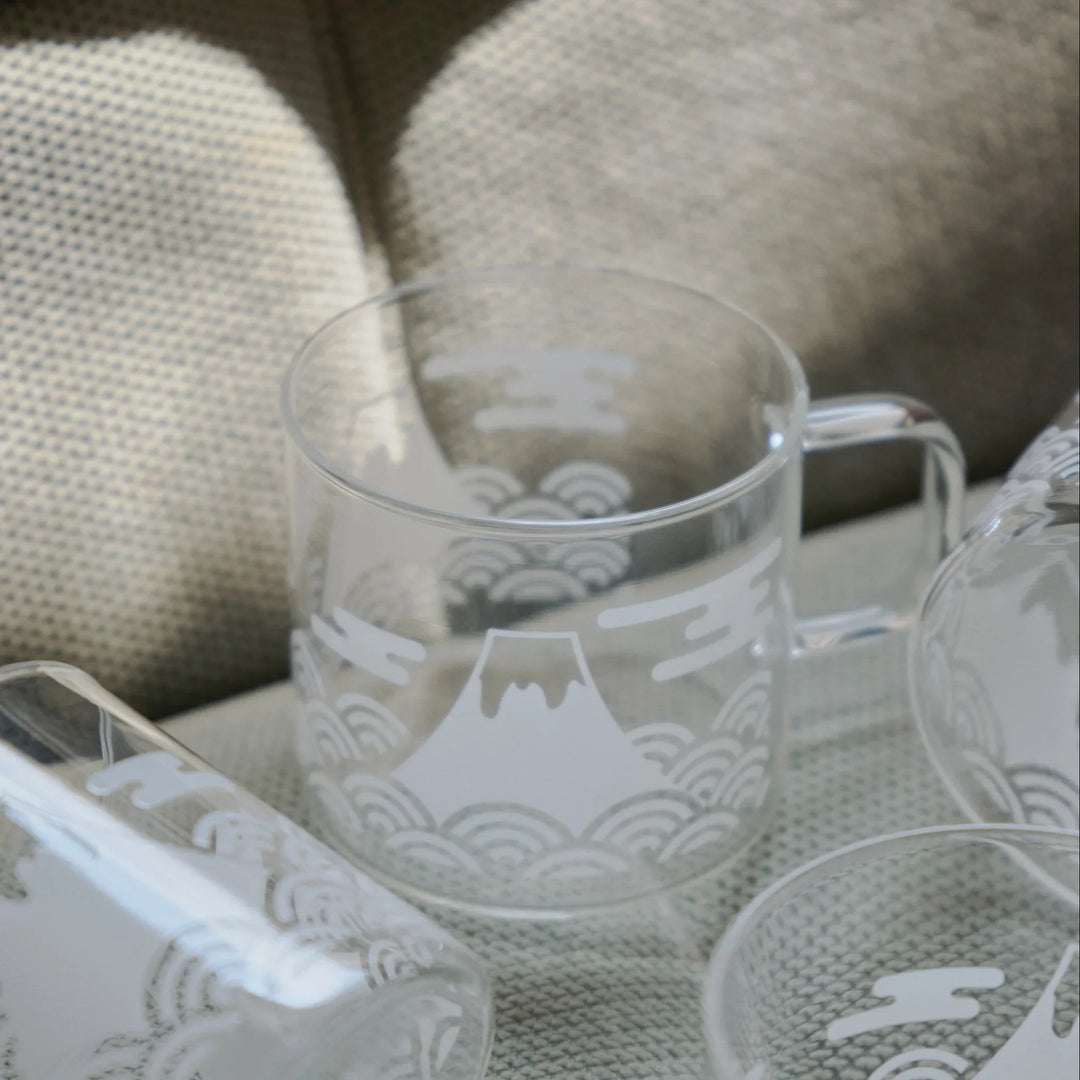Set of HARIO Mount Fuji thermochromic glass mugs with white traditional Japanese wave patterns on a textured armchair