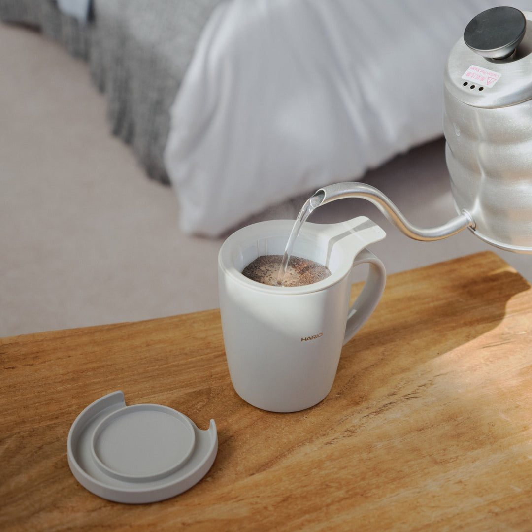 Resting mesh infuser filter on top of hario ceramic tea and coffee mug on a wooden bedroom table near books