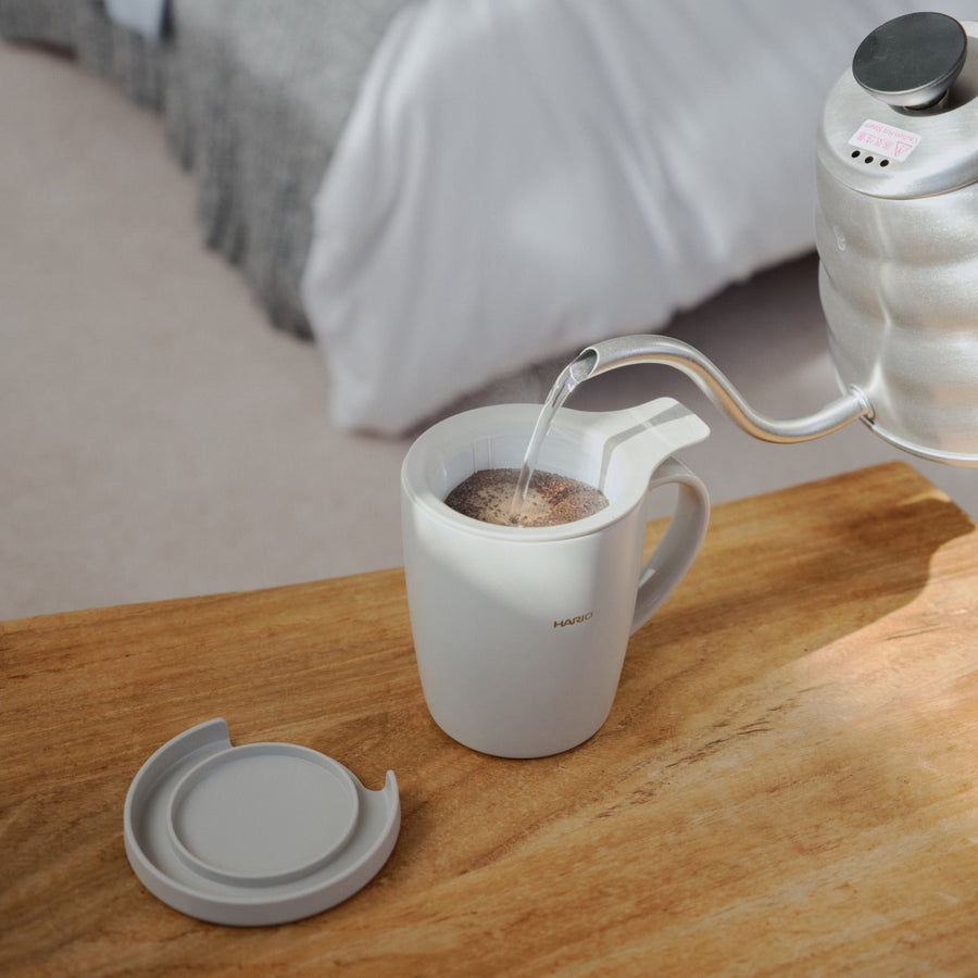Resting mesh infuser filter on top of hario ceramic tea and coffee mug on a wooden bedroom table near books