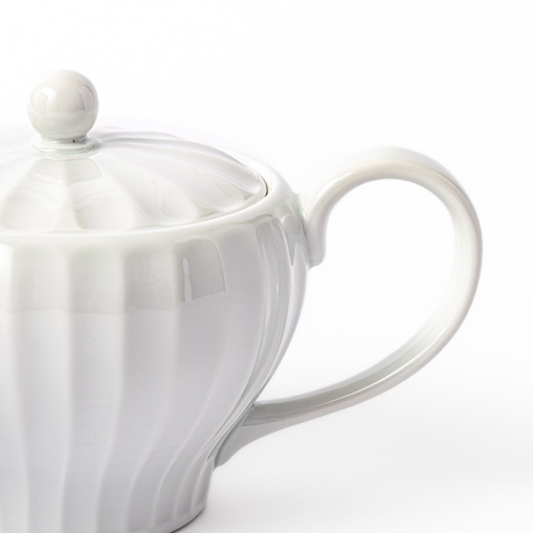 White teapot with vertical petal-inspired ridges and a round lid, perfect for a refined and elegant tea presentation.