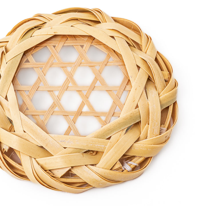 A round handwoven bamboo drink coaster showcasing a traditional star pattern weave and a braided natural fiber border