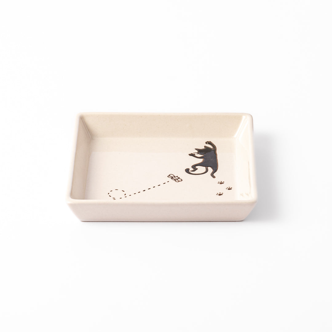 Square beige plate featuring a playful black cat chasing a butterfly, with paw prints and a dotted flight path.