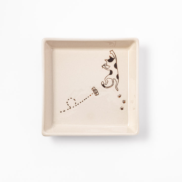 Beige square plate with playful calico cat and butterfly illustration, accented with dotted lines and paw prints.